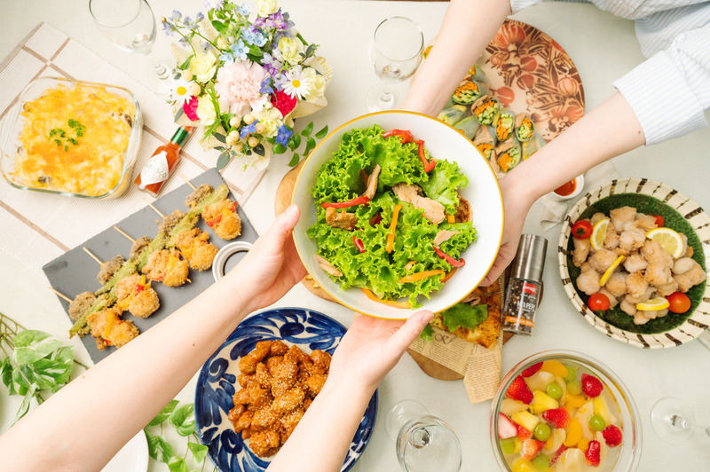 大豆ミートの串やサラダなど色鮮やかな料理を囲んで、手を伸ばし合う食卓のシーン。