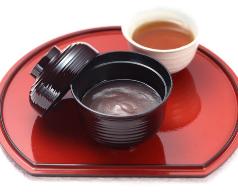 黒い和の器に盛られた磯駒海苔の葛汁粉とお茶。赤いお椀の上。