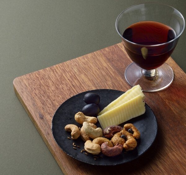 木製のボードにチーズと黒オリーブ、素焼き・味付けの大粒カシューナッツを盛り、赤ワインのグラスを添えて