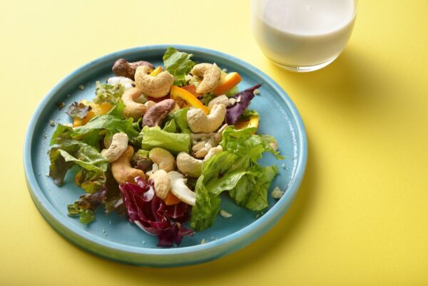— 大粒カシューナッツとオレンジ、彩り野菜を盛り付けたサラダを斜め上から撮影した写真、グラスのミルクを添えて